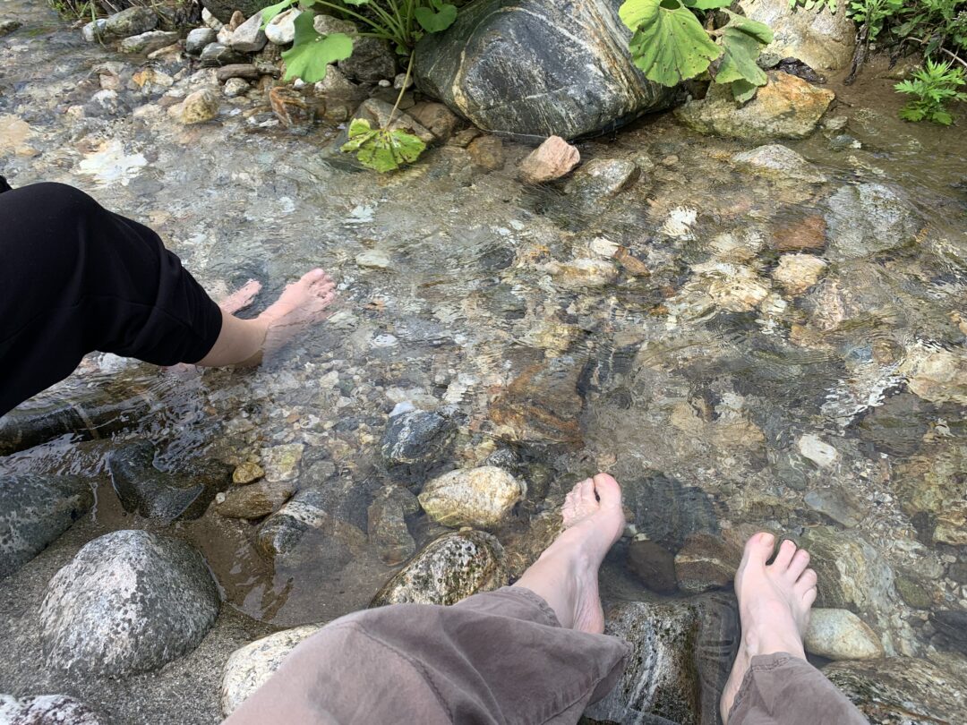 Due coppie di piedi in ammollo nelle limpide acque di un fiume di montagna dal fondo sassoso