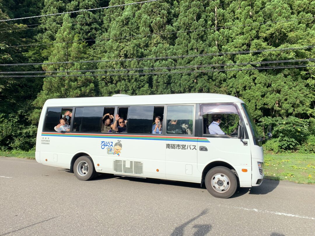 un piccolo autobus giapponese e ai finestrini persone affacciate a salutare