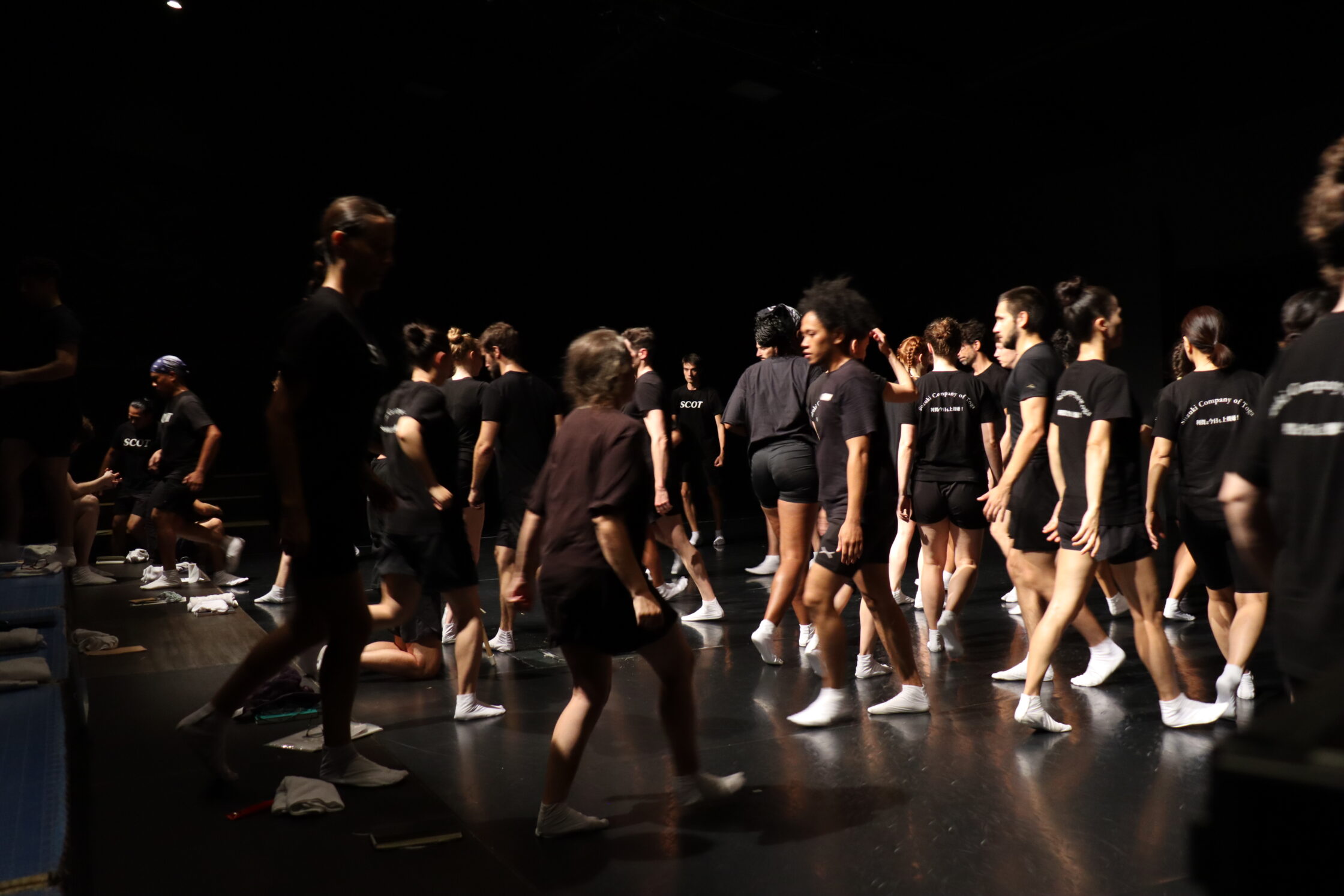 Un gruppo di persone che si sta muovendo nello spazio di una sala prove teatrale